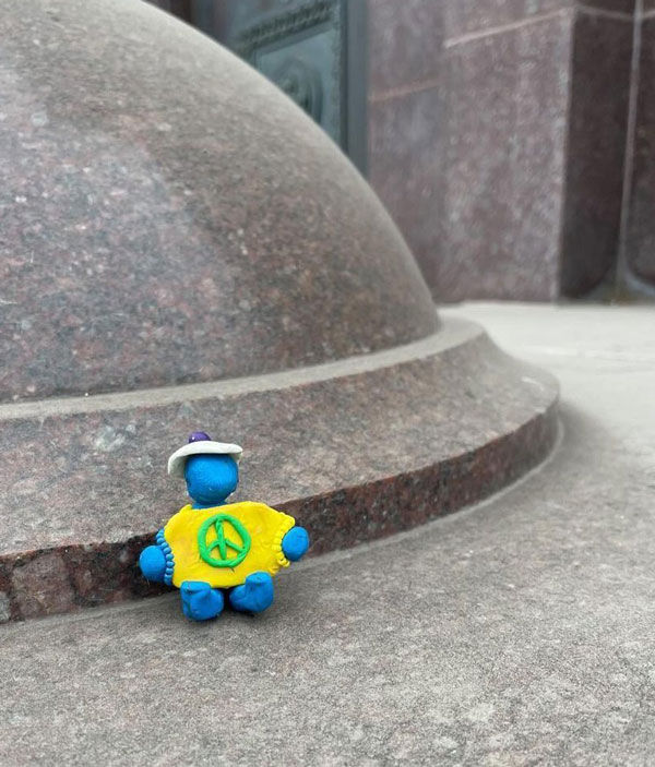 A blue figurine wearing a yellow T-shirt with a peace sign on it.