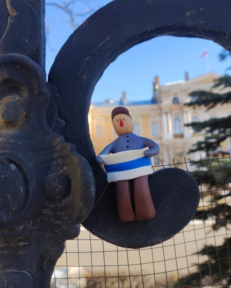 A figurine with an antiwar flag, perched on a fence.