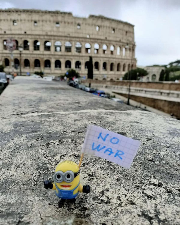 A yellow and blue minion figurine holds a poster that reads, “No War.”