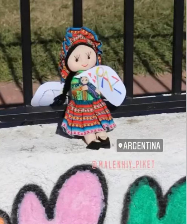 A picture of a multicolored rag doll holding a peace poster.