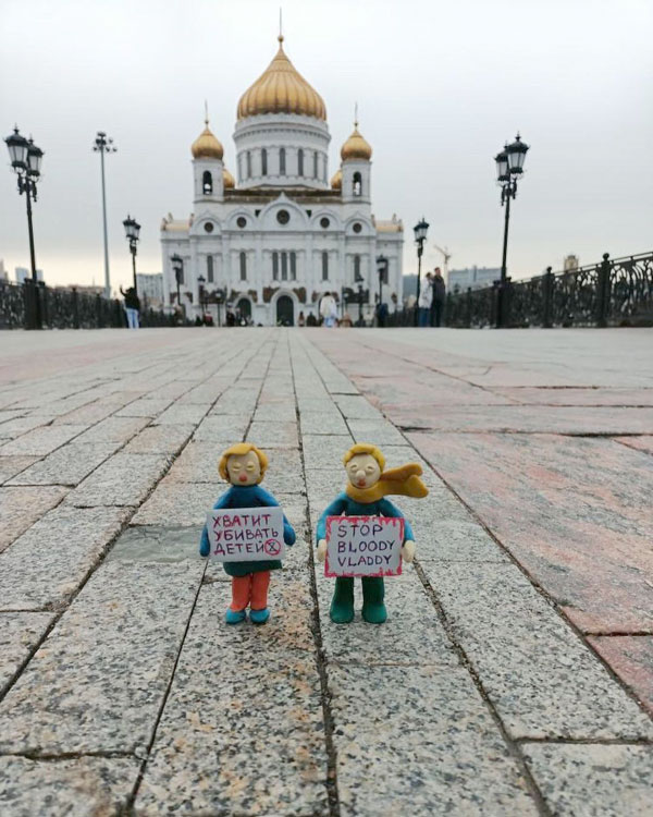 Two figurines standing in front of the Cathedral of Christ the Saviour in Moscow while holding antiwar posters. One reads, “Stop Killing Children,” the other, “Stop Bloody Vlady.”