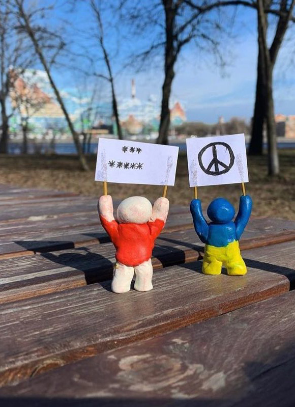 Two figurines holding antiwar posters, one with asterisks and the other with a peace symbol.