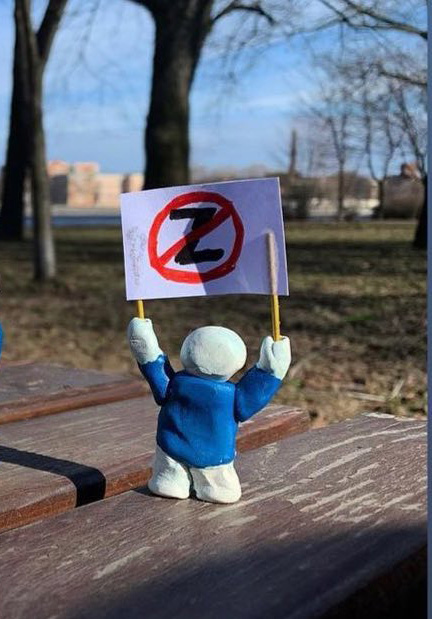 A figurine wearing a blue T-shirt holds a placard with a letter Z crossed out.