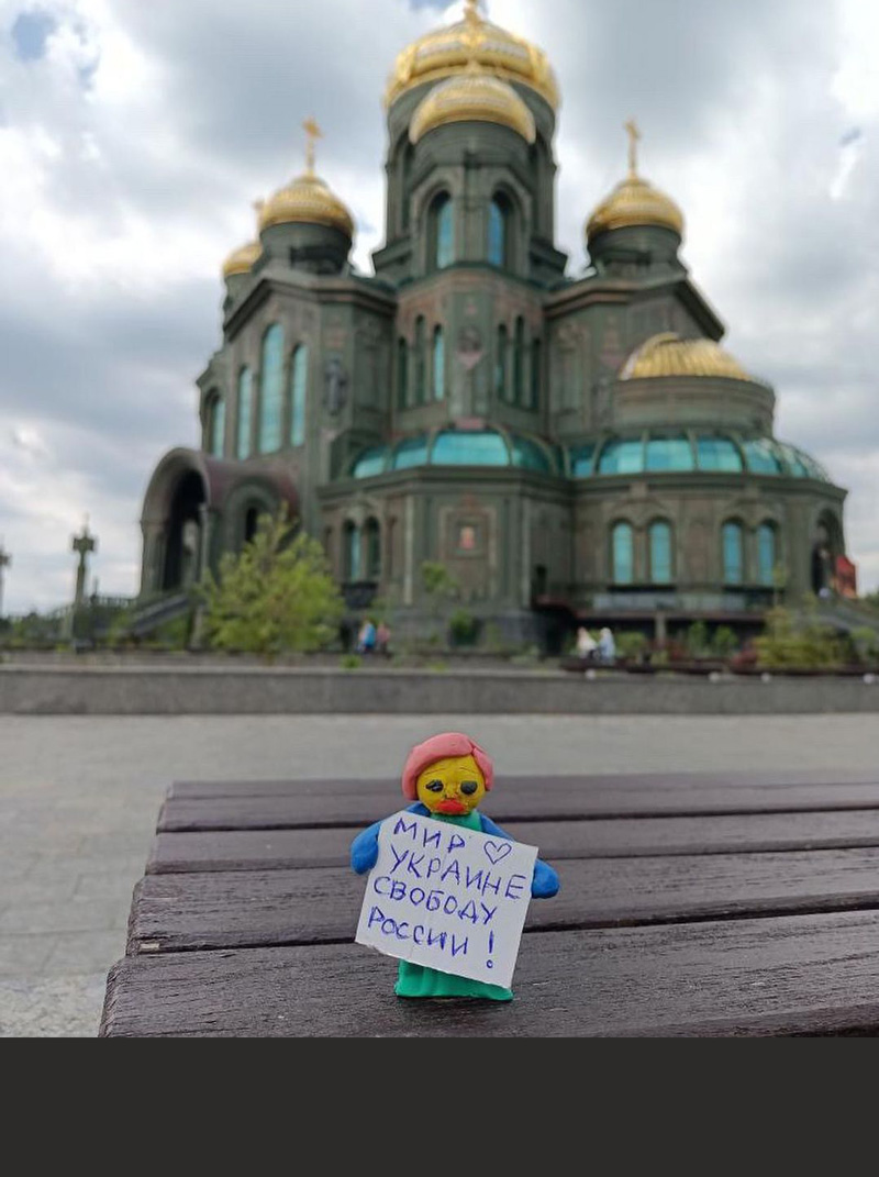 A figurine holding an antiwar poster in front of a cathedral.