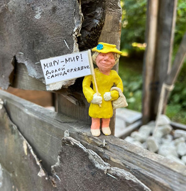 A figurine wearing a yellow dress and hat holds a white flag with antiwar inscriptions.